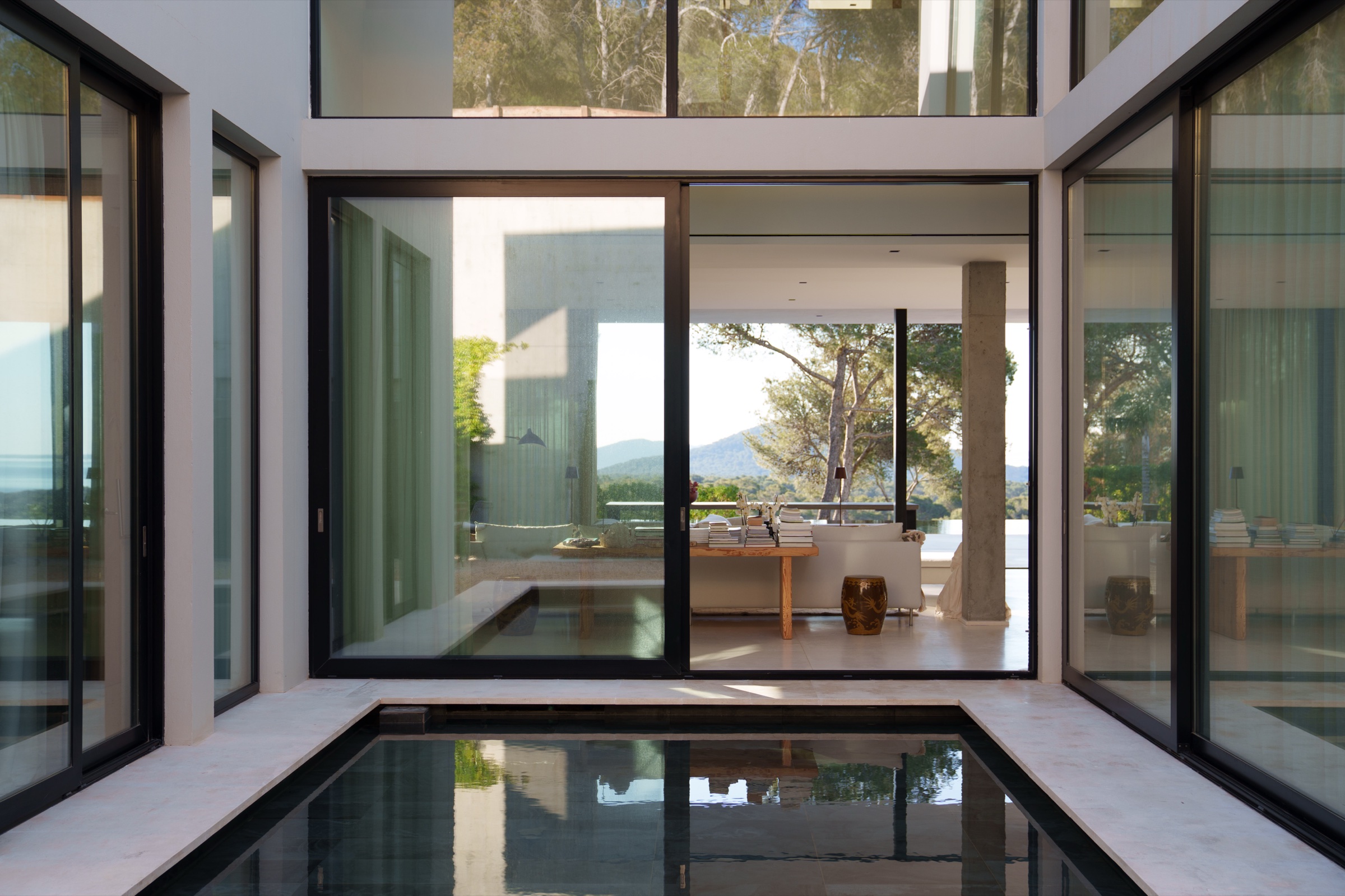 Glass-walled courtyard with a reflecting pool, opening onto a living space with mountain views