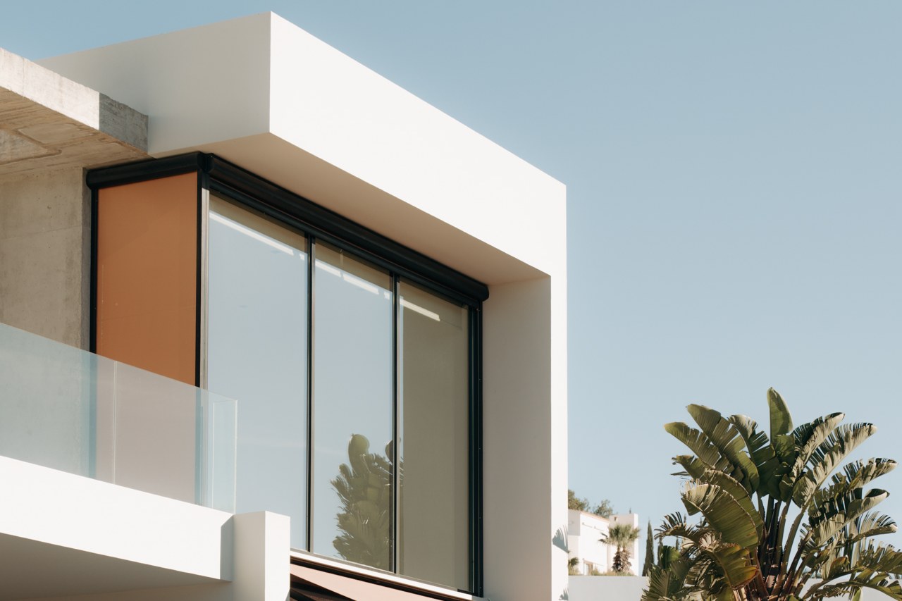 Contemporary villa exterior with a glass balcony rail and palm tree against a blue sky